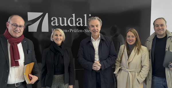 Foto vom Treffen bei audalis, die Beteiligten stehen vor Wand mit audalis Logo